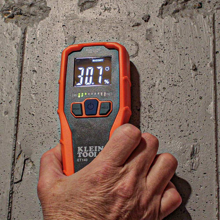Action shot of the ET140 moisture meter being pressed against a concrete wall. The device is set to masonry mode and displays a 30.7 percent relative moisture reading with yellow LED bars illuminated.