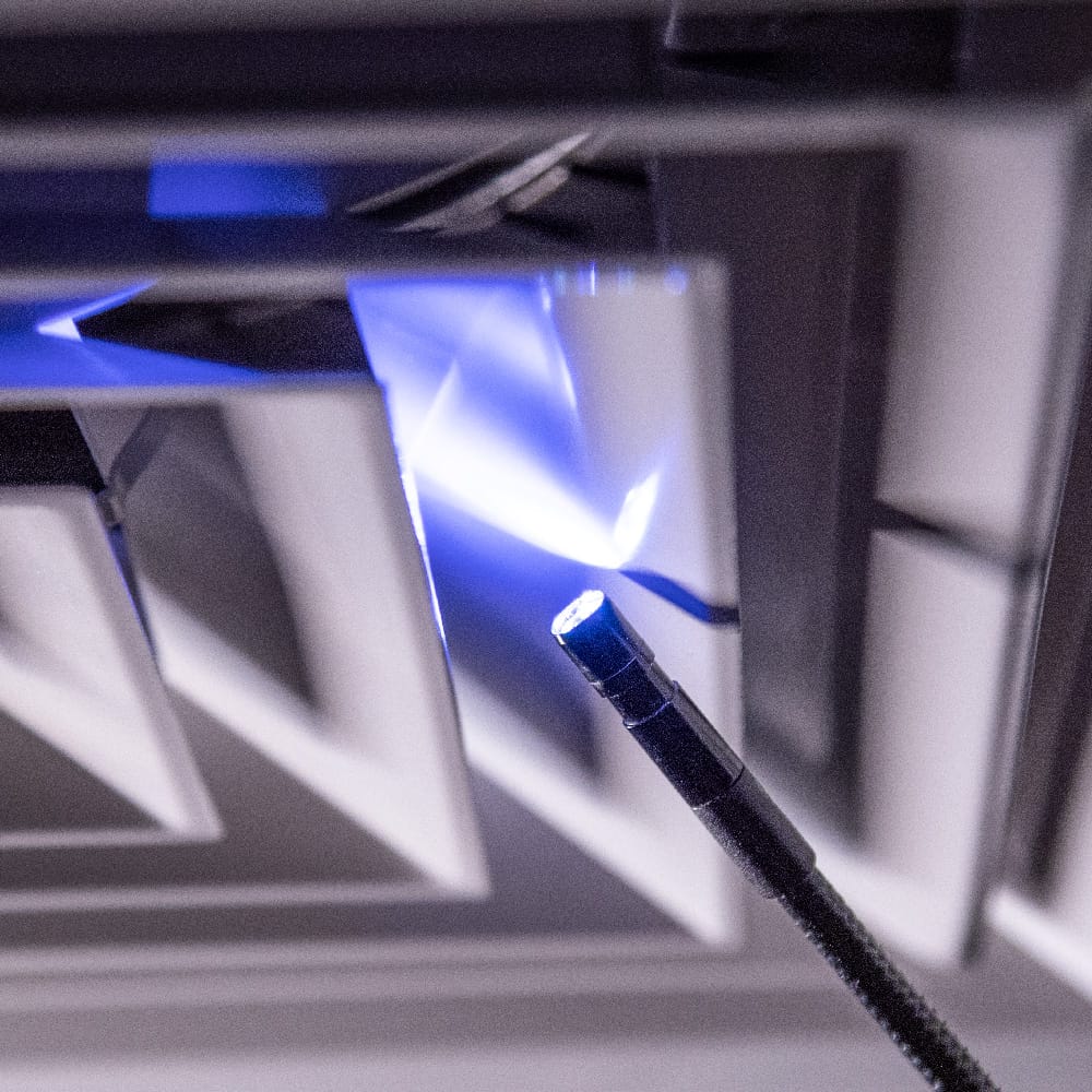 Close-up action shot of the 8mm borescope camera head navigating a metallic vent. The image highlights the intensity of the 6 integrated LEDs, which provide essential illumination for capturing clear diagnostic details in dark, confined spaces.