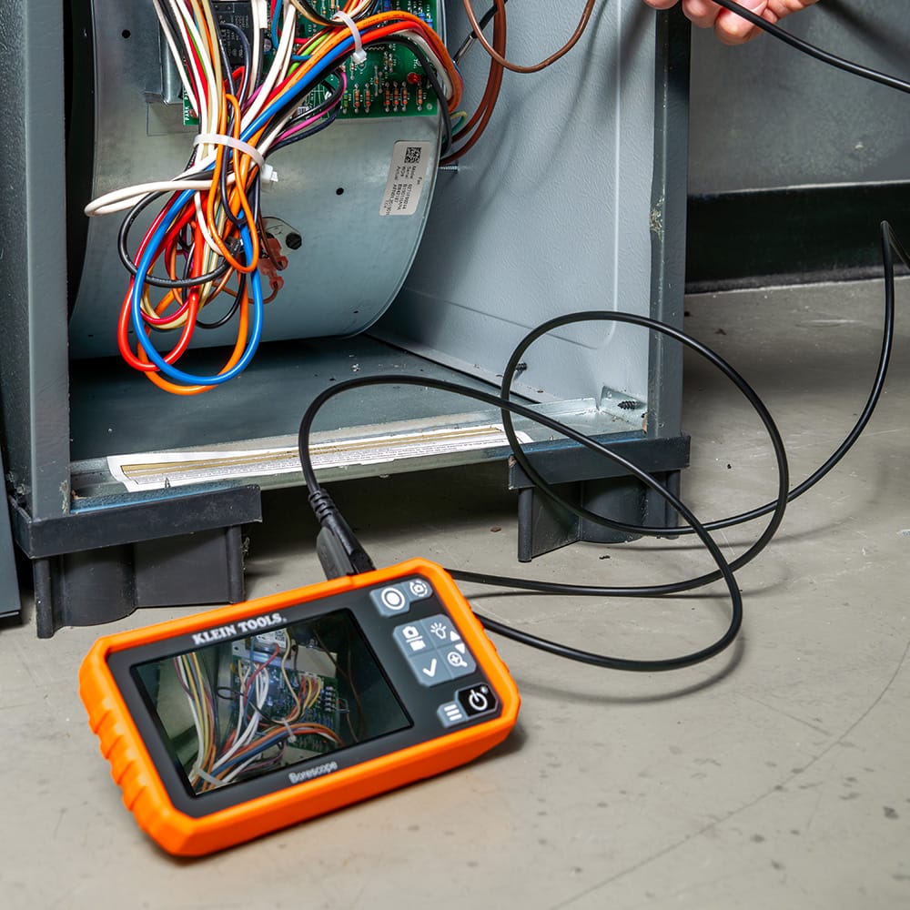 Action shot of a professional technician using the ET17 utility borescope to inspect a furnace blower and wiring harness. The 4.3-inch high-resolution color screen provides a clear view of internal mechanical components, demonstrating the tool's effectiveness for HVAC system diagnostics.