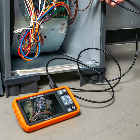 Action shot of a professional technician using the ET17 utility borescope to inspect a furnace blower and wiring harness. The 4.3-inch high-resolution color screen provides a clear view of internal mechanical components, demonstrating the tool's effectiveness for HVAC system diagnostics.