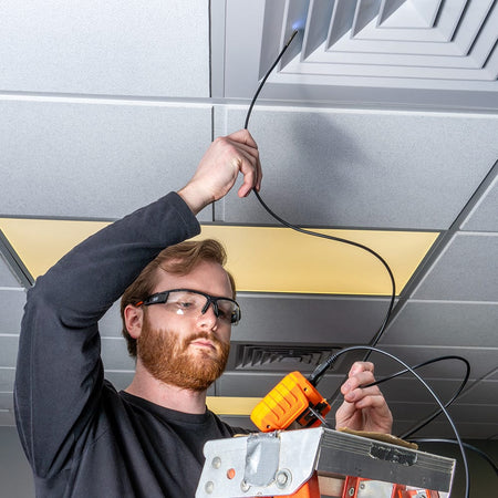 Action shot of an HVAC professional standing on a ladder using the ET17 borescope to inspect an overhead ceiling air register. The technician uses the 10-foot nylon snake to reach high into the ductwork while monitoring the 720p HD video feed on the handheld display.