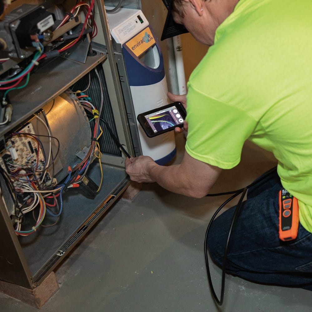 Action shot showing an HVAC professional using the ET20 borescope to inspect the internal blower motor and wiring of a furnace. The clear 640 x 480 image is displayed on a mobile device, allowing for instant system diagnosis without disassembling equipment.