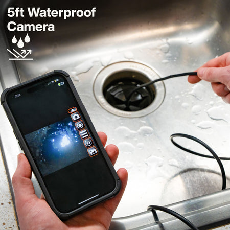 Action shot of a technician using the 5-foot waterproof camera to inspect a kitchen sink drain, with the live video feed displayed simultaneously on a smartphone screen.