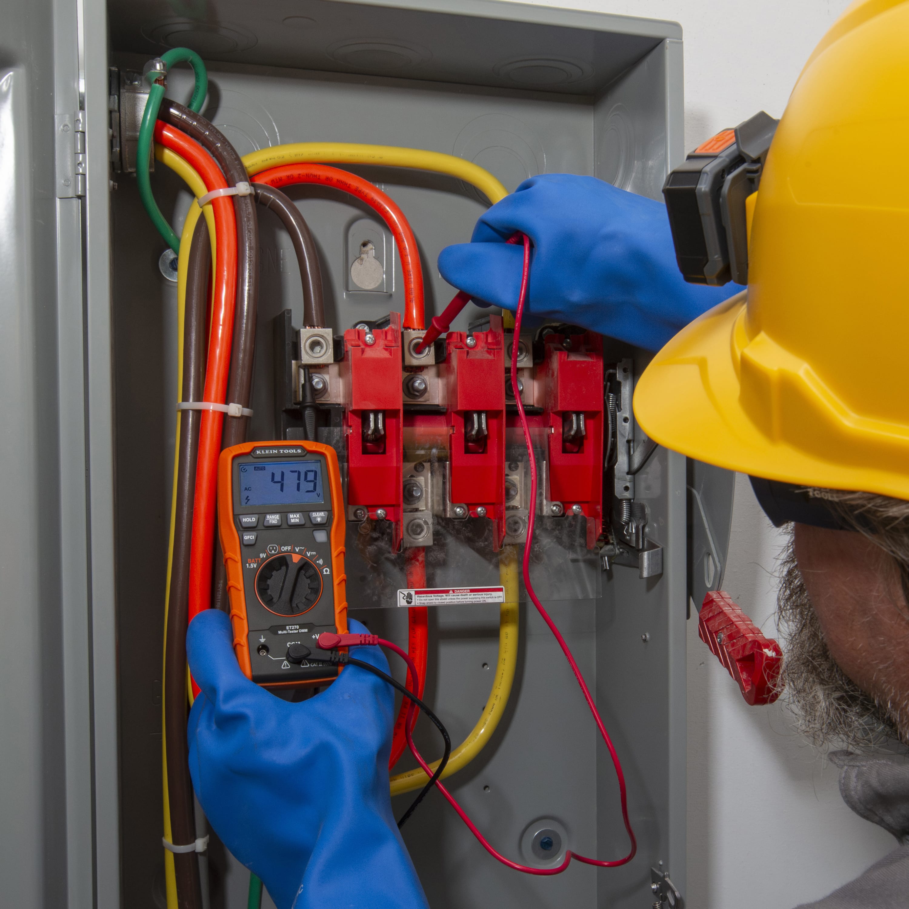 A professional electrician wearing a hard hat and insulated safety gloves uses the ET270 multimeter to test a high-voltage electrical disconnect. The meter display shows a reading of 479V AC, demonstrating its reliability for industrial electrical troubleshooting.