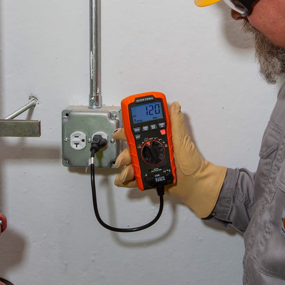 A technician using the Klein Tools ET270 digital multimeter to test a standard 120V AC outlet. The display shows a voltage reading of 120V while simultaneously identifying an open ground wiring fault, demonstrated by the clear "Open Grd" indicator and a red alert light.