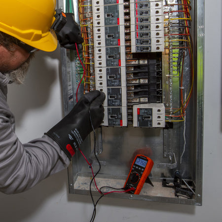 An electrician in a hard hat and protective high-voltage gloves uses the ET270 multimeter to probe a residential circuit breaker panel. The meter is placed at the base of the panel box and displays a steady reading of $275.0V$, illustrating its use in multi-phase electrical environments.
