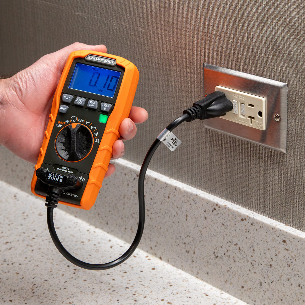 Close-up of the Klein Tools ET270 performing a GFCI trip test on a kitchen or bathroom style receptacle. The user is pressing the dedicated GFCI button, and the high-contrast display shows a trip time of 0.10 seconds, confirming the safety device is operating within specifications.