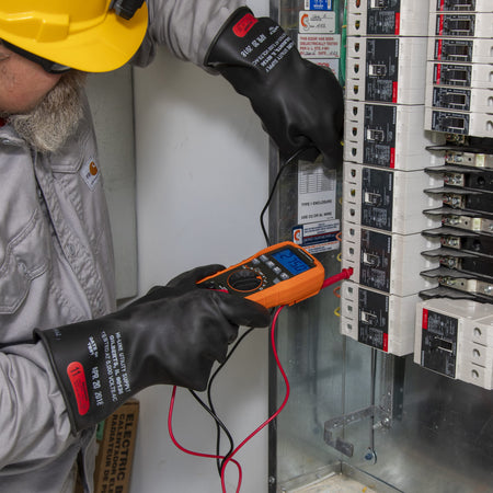 Professional application shot of the ET270 multimeter being used by a tradesman to troubleshoot a row of circuit breakers. The technician is wearing safety gear while using the red and black test leads to verify voltage across individual breakers in a complex electrical panel.