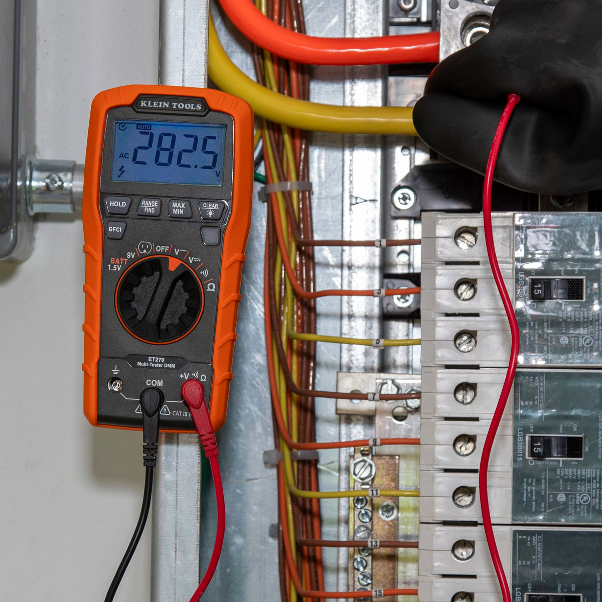 Close-up detail of the ET270 multimeter display showing $282.5V$ AC while testing industrial-grade circuit wiring. The image highlights the auto-ranging feature and the secure connection of the right-angle test leads into the common and voltage input jacks.