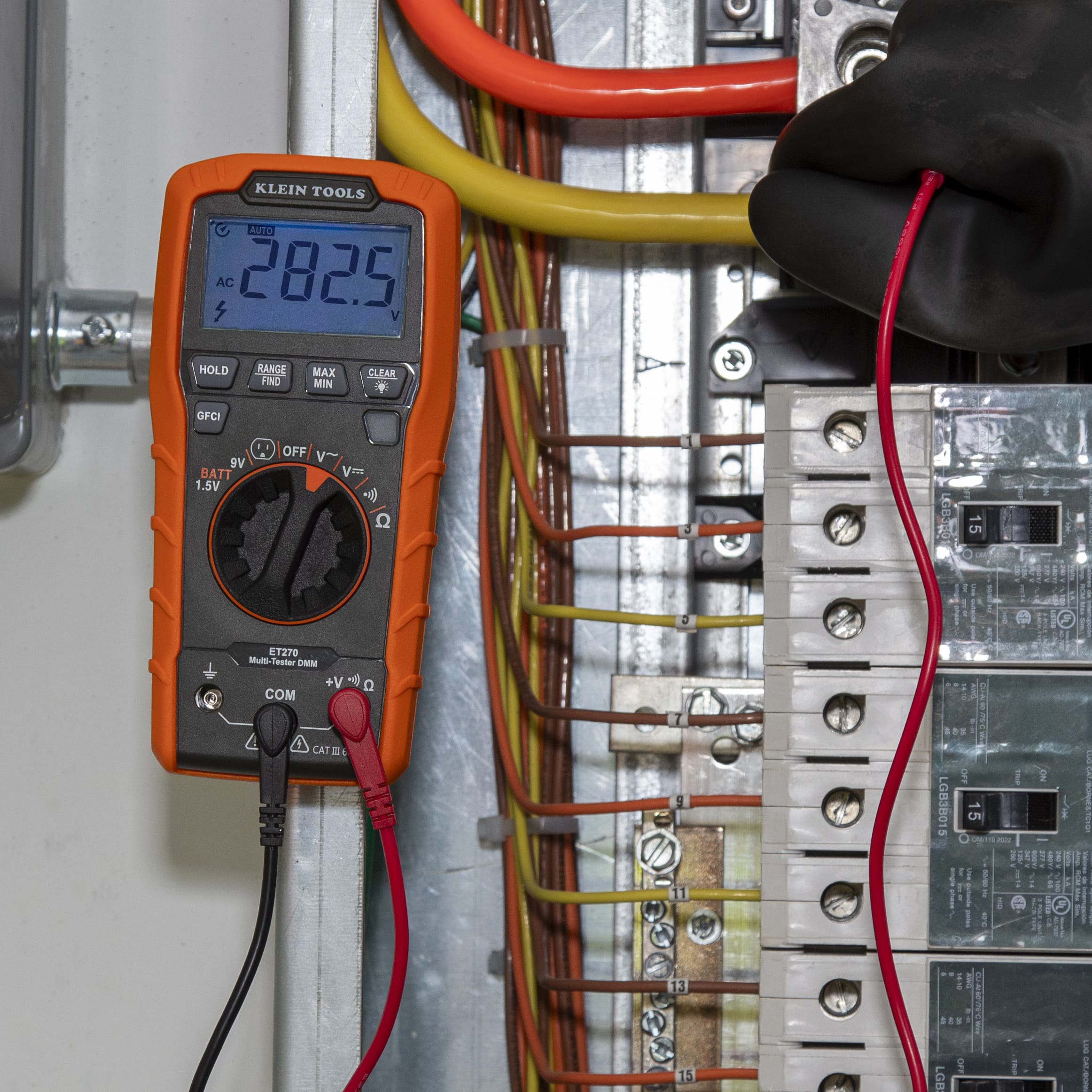 Close-up detail of the ET270 multimeter display showing $282.5V$ AC while testing industrial-grade circuit wiring. The image highlights the auto-ranging feature and the secure connection of the right-angle test leads into the common and voltage input jacks.