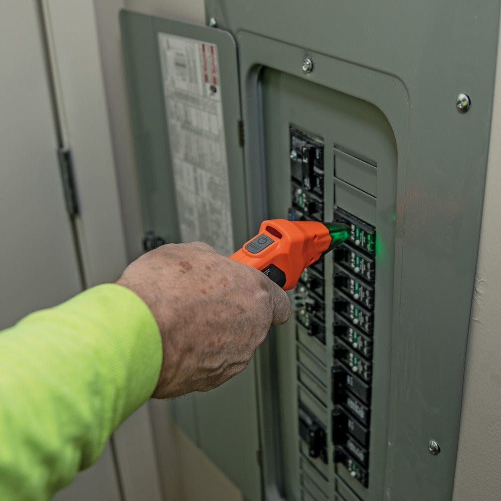A close-up of a hand holding the orange receiver wand to scan a column of circuit breakers in a grey electrical panel, with the tip illuminated green.