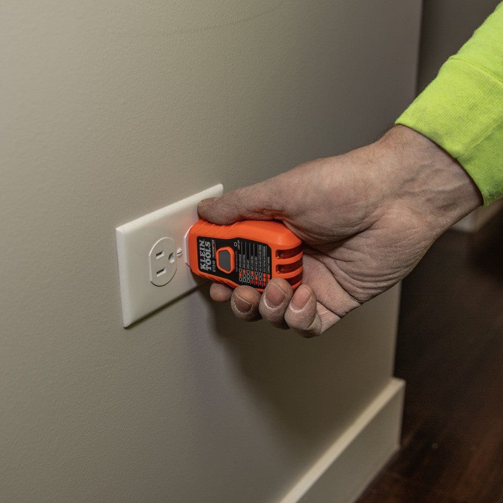 A close-up of a hand plugging the orange transmitter unit into a standard white electrical outlet to trace the circuit.
