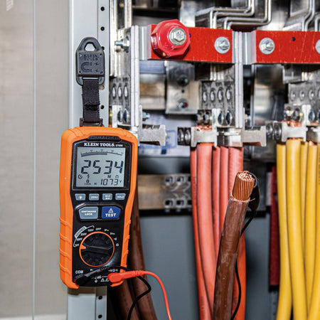 A professional application shot showing the ET600 megohmmeter suspended by a magnetic hanger inside a heavy-duty electrical cabinet. The meter is shown connected to thick gauge industrial wiring, monitoring a test voltage of 1073V DC.