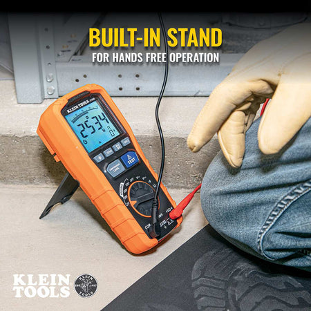 An action shot of the ET600 megohmmeter being used in a hands-free application. The device is supported by its integrated heavy-duty kickstand on a concrete surface, allowing a technician wearing safety gloves to monitor insulation resistance readings while managing the test leads.