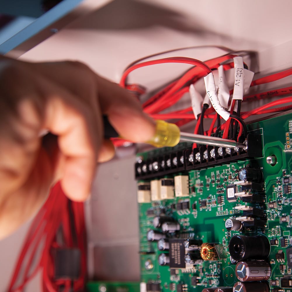 Technician using the extended-reach Klein 32614 driver to tighten wire connection screws on an electronic circuit board module.