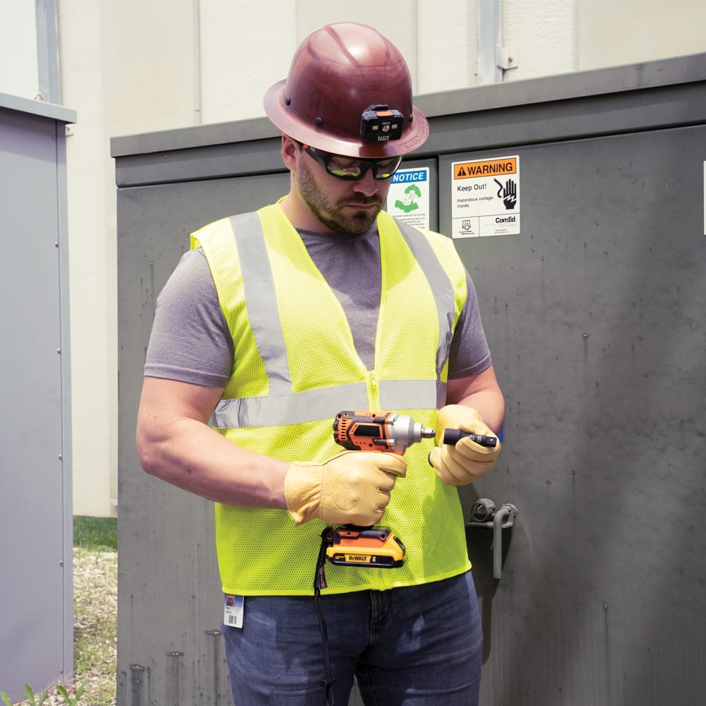 Utility technician standing at an outdoor transformer cabinet holding a Klein impact wrench equipped with the 66080 socket.