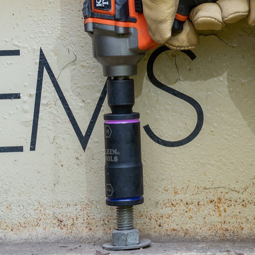 Electrician using an impact wrench with a Klein 66078 large adapter and flip socket to drive an anchor bolt nut into concrete.