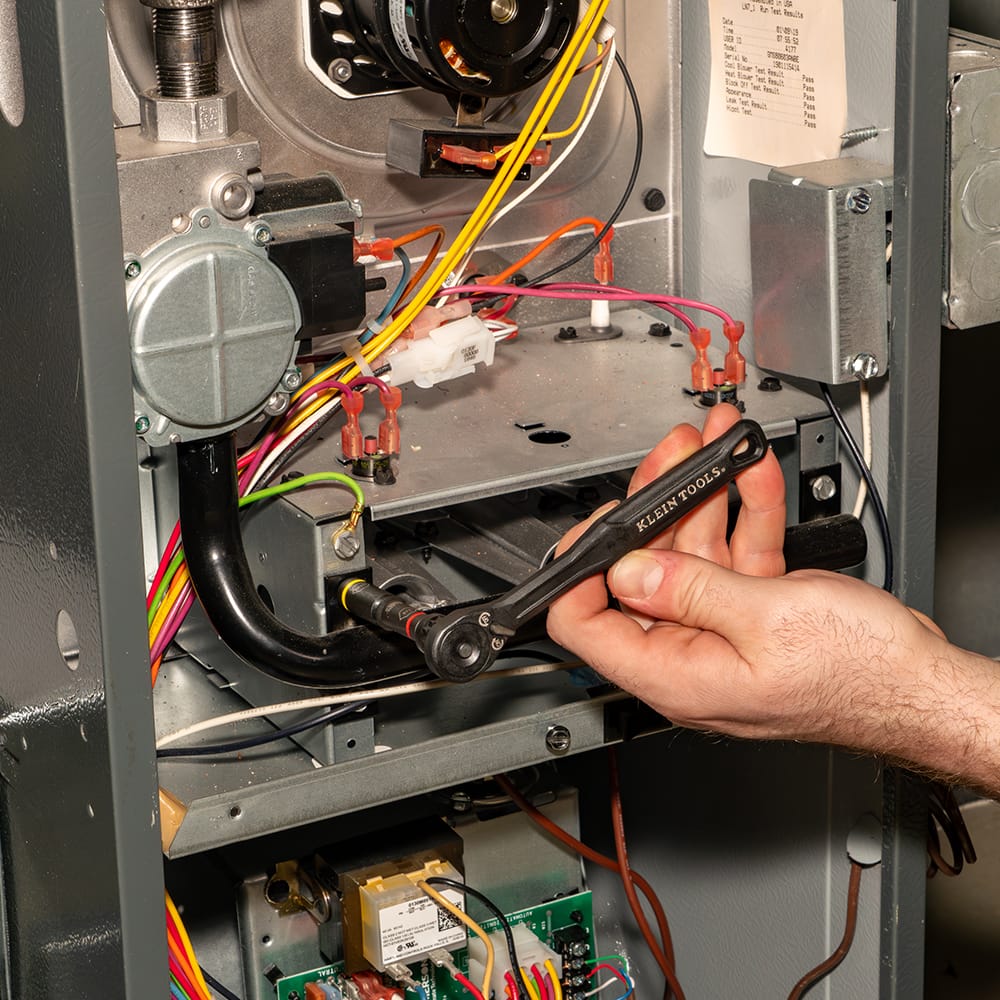 Technician using the Klein 65238 low-profile ratchet with a flip socket to adjust hardware inside a tight HVAC electrical equipment compartment.