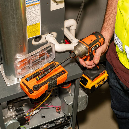 HVAC technician driving a hex head screw on a furnace cabinet using an impact driver equipped with the Klein 65238 flip socket shaft setup.