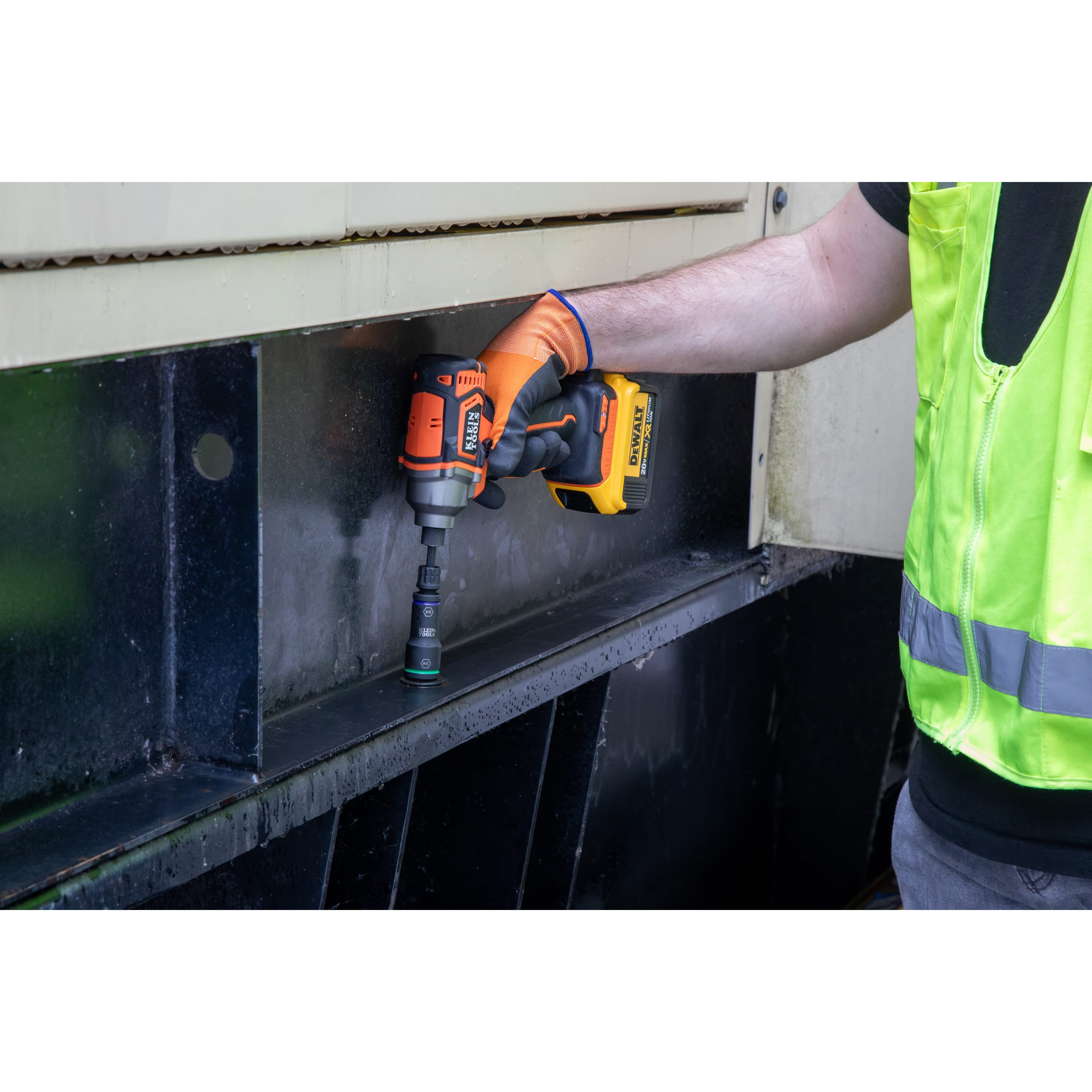 Worker using an impact driver with a Klein 3/4-inch flip socket to fasten a structural steel beam bolt on an industrial equipment housing.