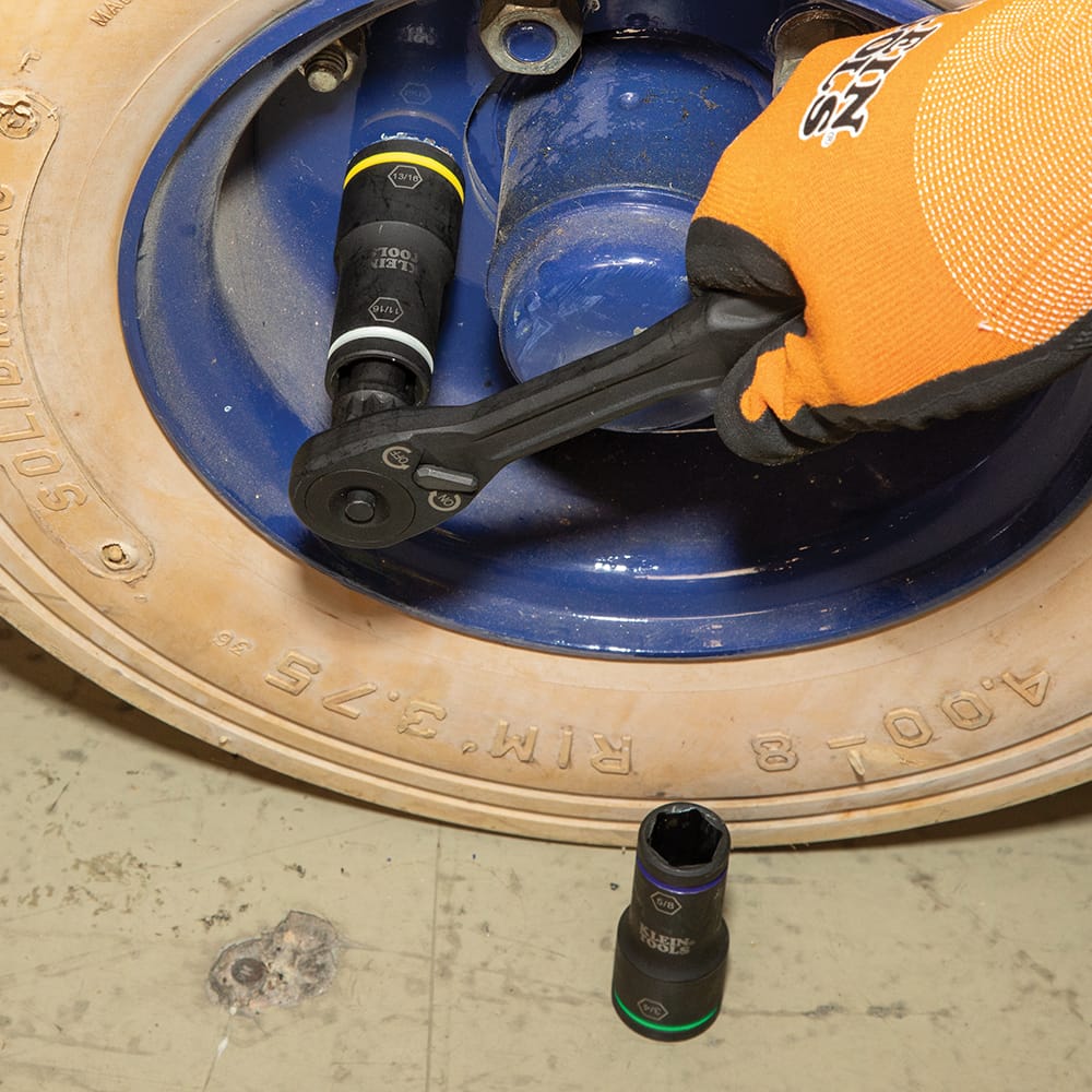 Mechanic using a ratchet equipped with an 11/16-inch Klein flip socket to loosen a heavy steel lug bolt on an equipment wheel assembly.