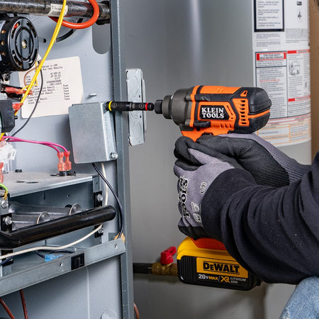 Technician using a power impact driver with a Klein 5/16-inch flip socket to fasten a grounded electrical box inside an HVAC furnace unit.
