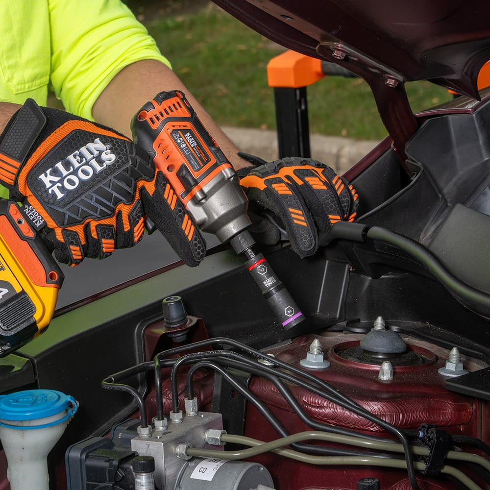 Technician using an impact driver with a Klein 12 mm x 14 mm flip socket to adjust suspension mounting bolts inside an engine bay.