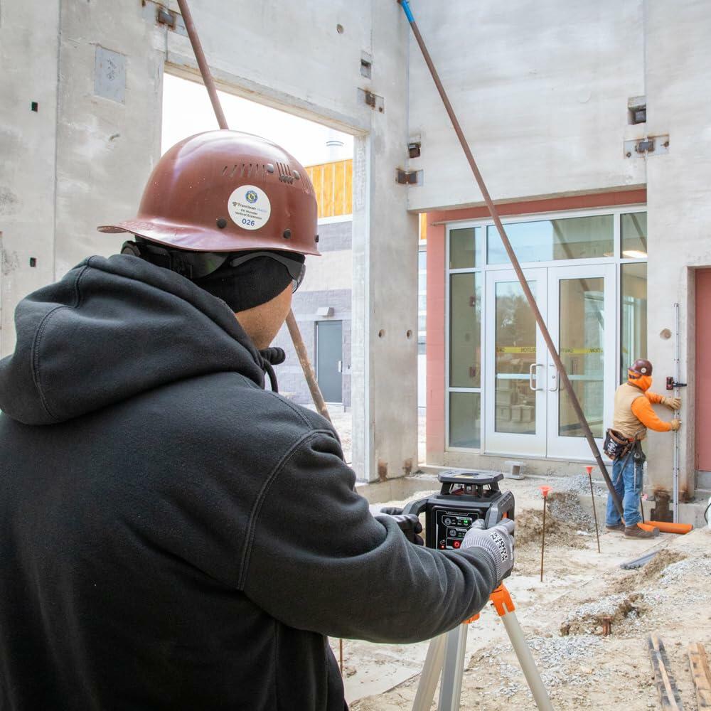 Two construction workers using surveying instruments, including a tripod-mounted laser level, to perform alignment and measurement tasks on a concrete structure.