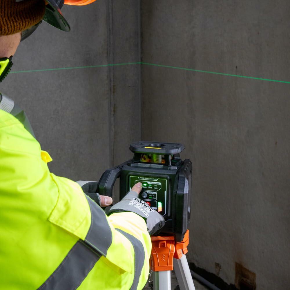 Operator adjusting settings on Klein Tools laser level mounted on tripod, with visible control panel for power and laser intensity at a construction site.