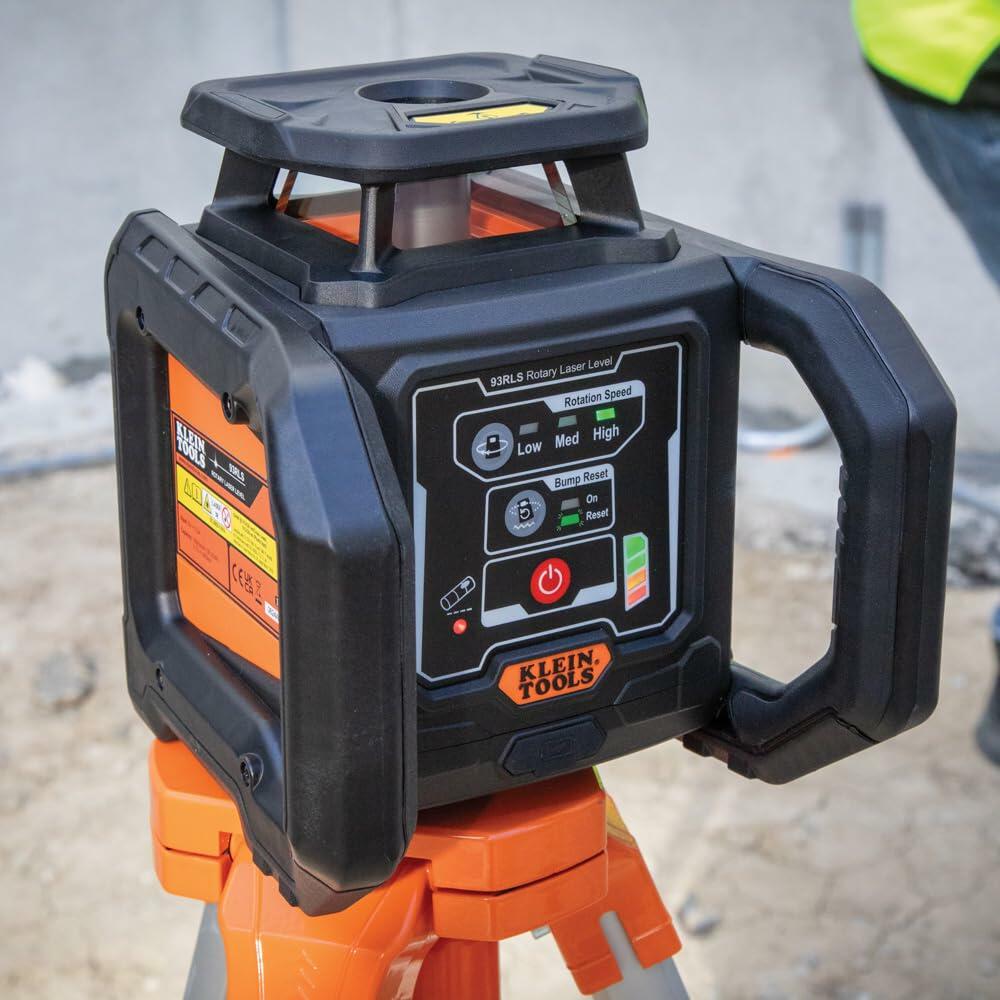 Klein Tools 93LPL rotary laser level mounted on tripod, with control panel and rugged casing, in use at an active construction site.
