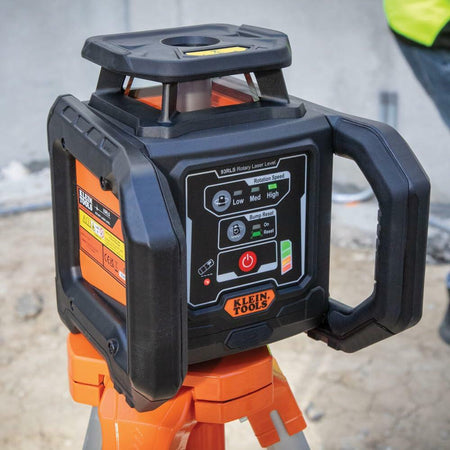 Klein Tools 93LPL rotary laser level mounted on tripod, with control panel and rugged casing, in use at an active construction site.