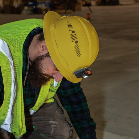 Contractor wearing a Klein 60262 yellow vented hard hat with a front-mounted LED headlamp inspecting low-light commercial floor surfaces.