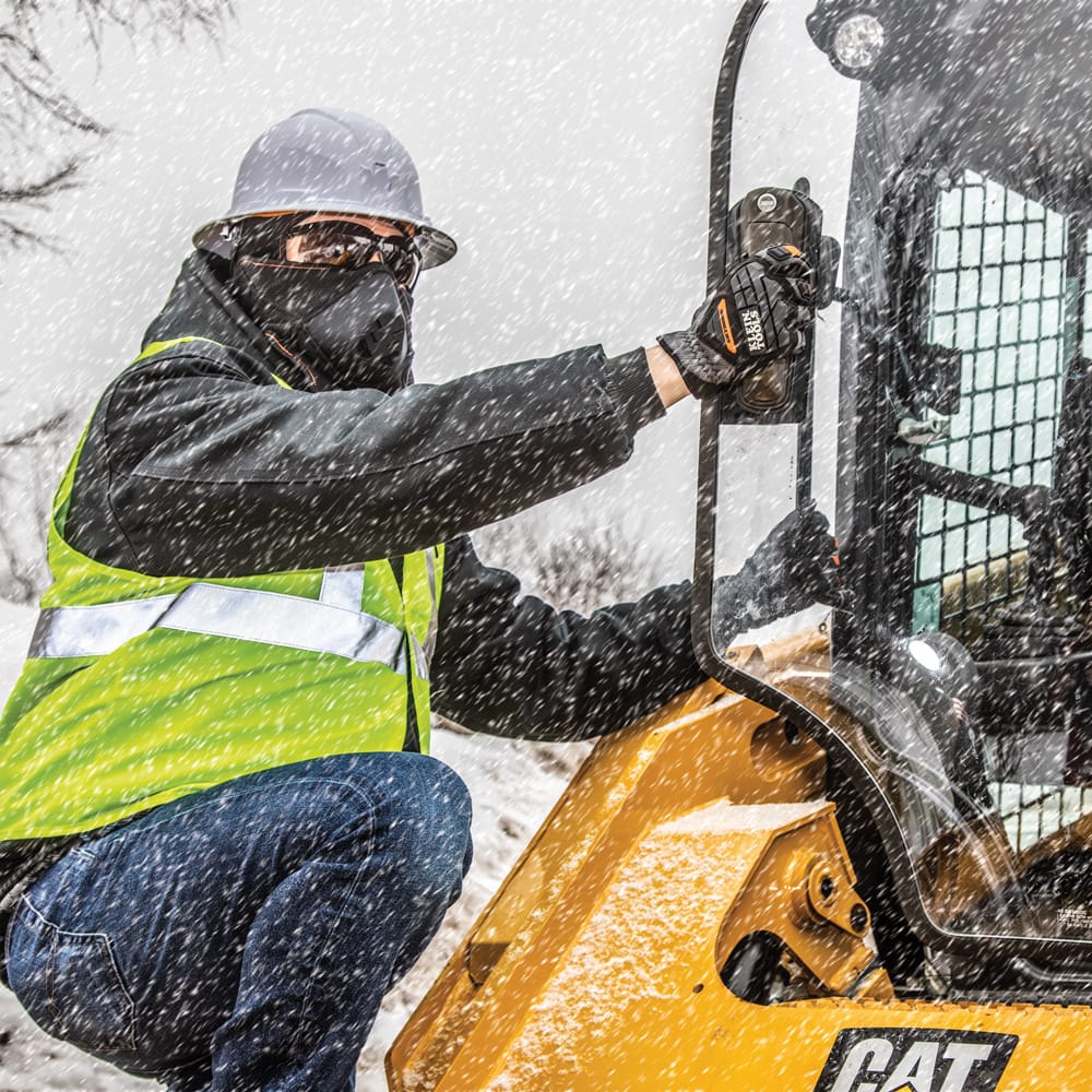 Construction worker wearing the Klein 60400 white hard hat while operating heavy machinery outdoors during winter snowfall.