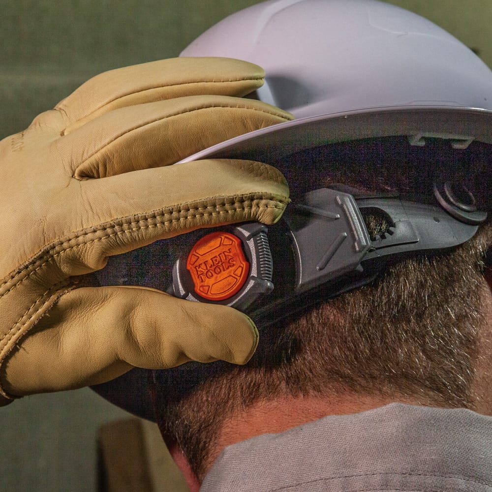 Gloved worker turning the oversized rear ratchet dial on the Klein 60400 hard hat for easy one-handed fit adjustment on job sites.