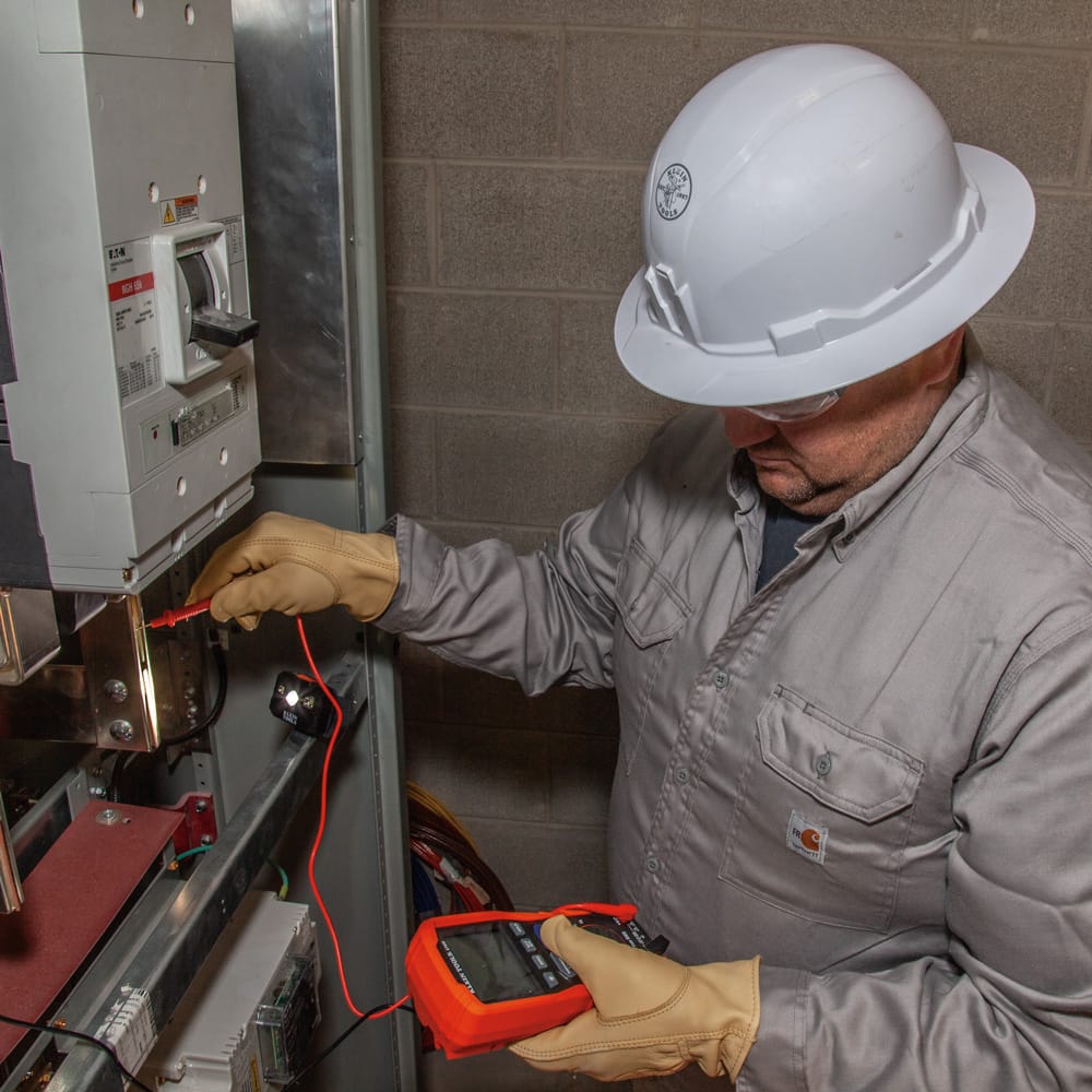 Electrician wearing the Class E non-vented Klein 60400 hard hat while performing high-voltage switchgear testing for 20kV electrical safety.