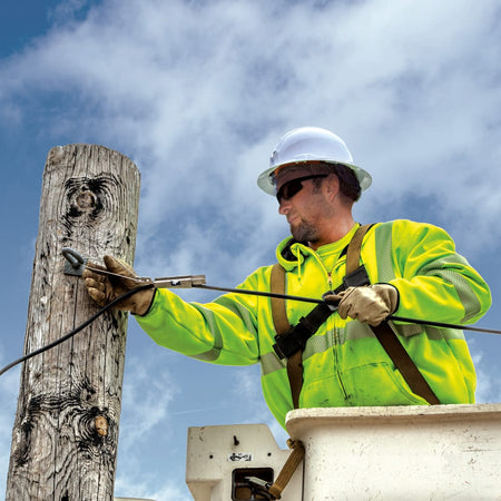 Utility lineworker wearing the Klein 60400 full brim hard hat in a bucket truck for overhead impact and sun protection while servicing power lines.