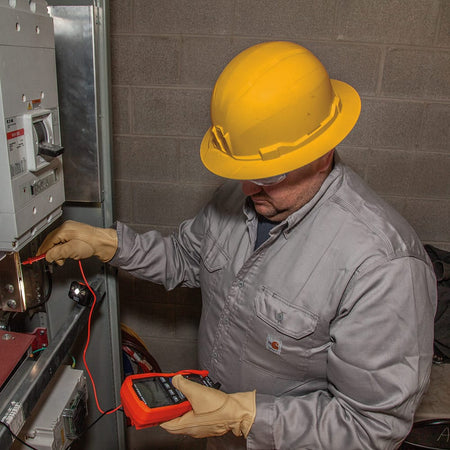Electrician wearing a Class E non-vented Klein 60489 hard hat while testing high-voltage switchgear components for 20kV dielectric safety.