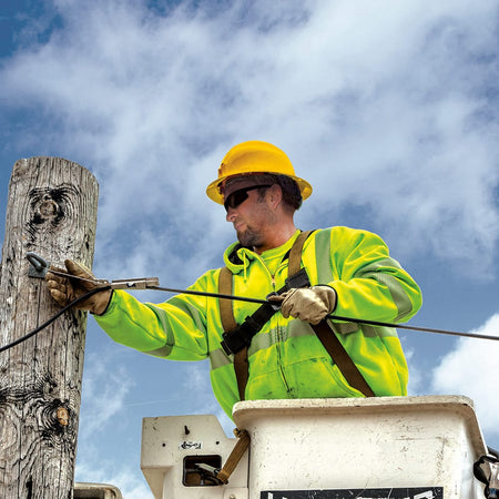 Utility lineworker wearing a high-visibility yellow Klein 60489 full brim hard hat in a bucket truck while securing overhead power lines.