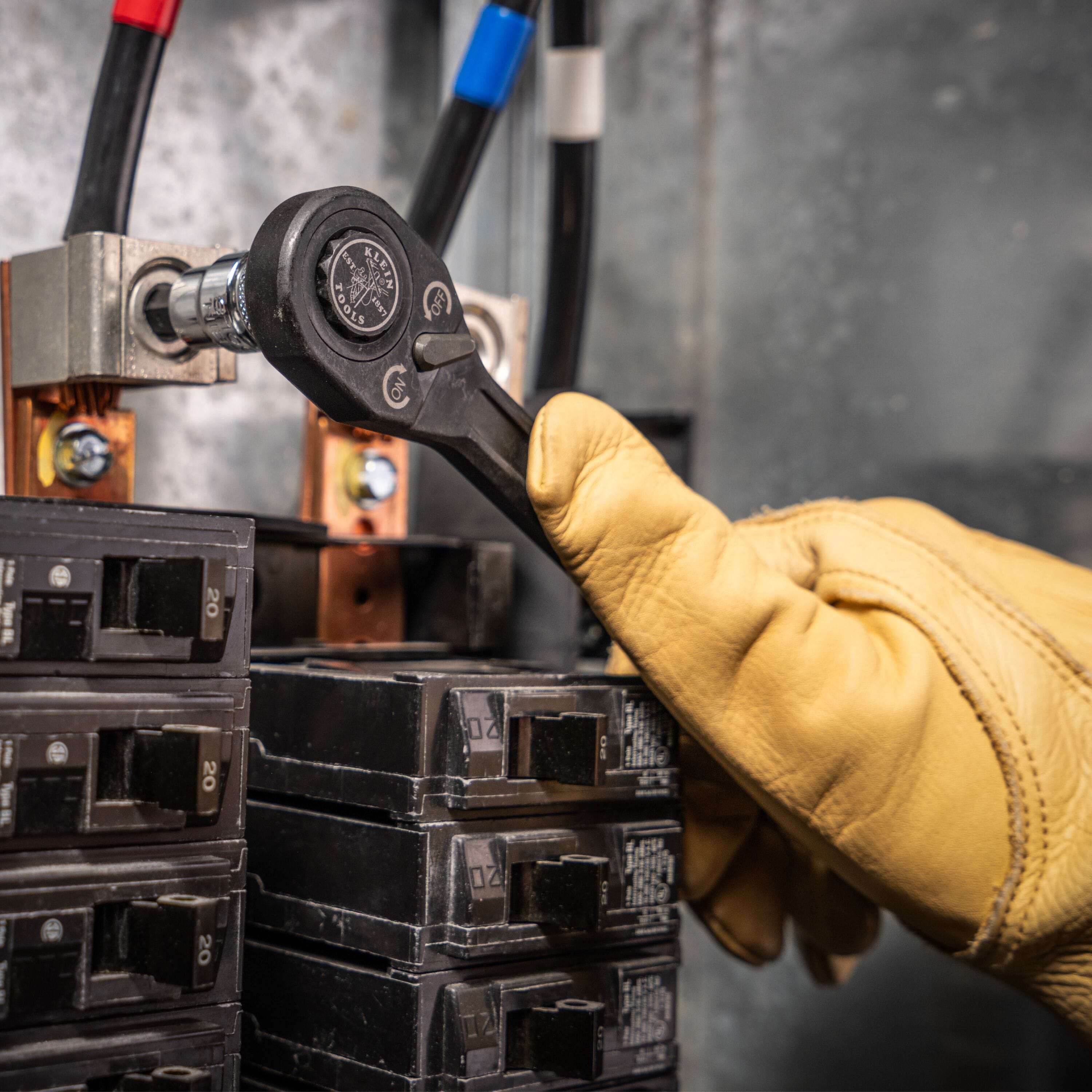Electrician using a ratchet with a Klein metric hex bit socket to secure a terminal lug inside a high-voltage electrical breaker box.