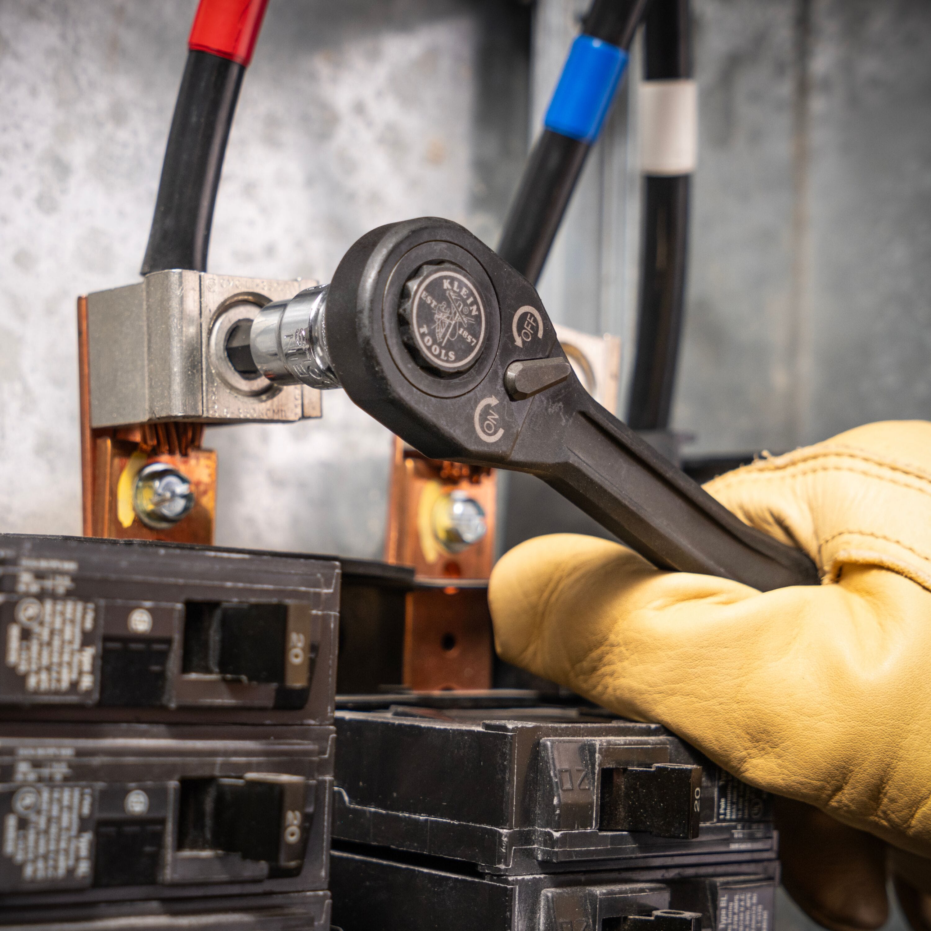 Electrician using a ratchet with a Klein hex bit socket to tighten a copper terminal lug bolt inside an electrical breaker panel.