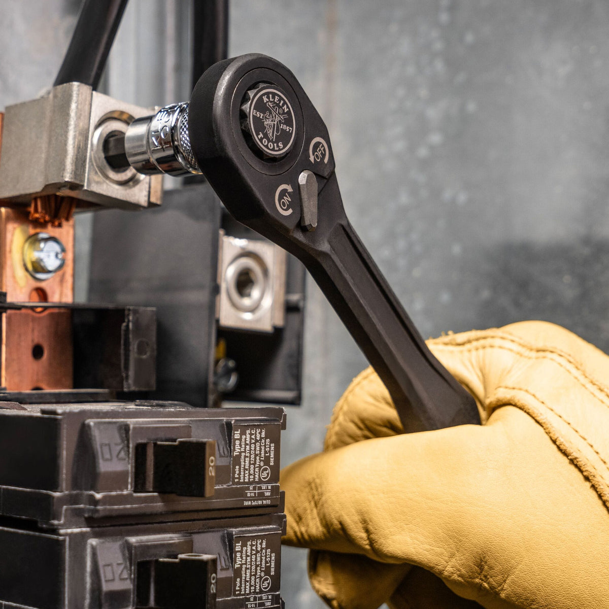 Technician using a ratchet and Klein hex bit socket to adjust an electrical lug connector inside a commercial breaker panel.