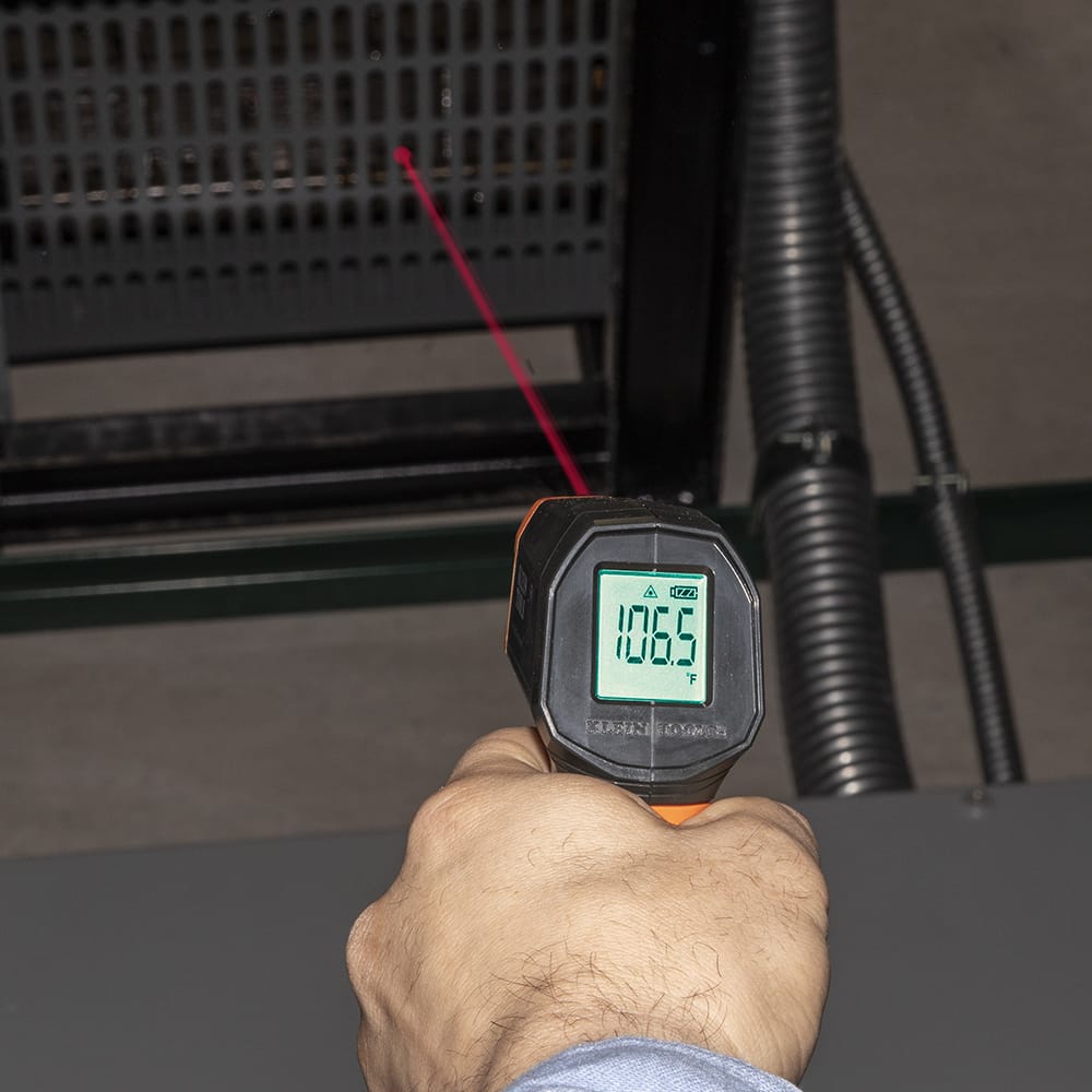 Top-down view of the Klein Tools IR1 focusing on the measurement aperture and targeting laser output. The image emphasizes the safety warnings and the precise alignment required for non-contact temperature diagnostics on electrical components.