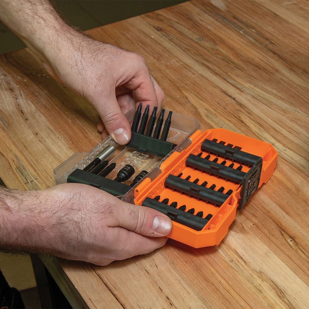 Worker swapping bit bars in the Klein MODbox storage case on a wooden workbench for fast bit selection on the jobsite.
