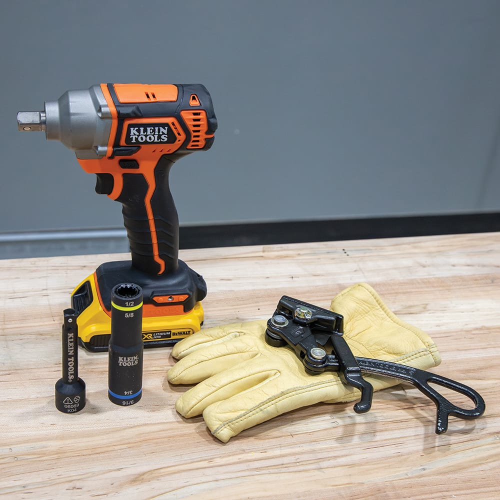 Klein 4-in-1 quad impact socket and drive extension adapter displayed on a workbench beside a cordless impact wrench and work gloves.