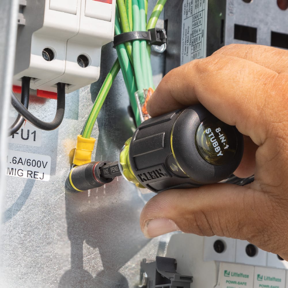 Technician using a Klein stubby driver fitted with the 32766 magnetic flip socket to tighten a ground terminal lug inside a cabinet.