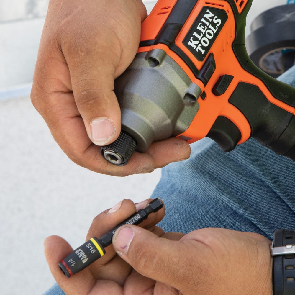 Worker holding the compact 3-inch Klein 32766 magnetic flip socket attachment next to a quick-release impact driver collar.