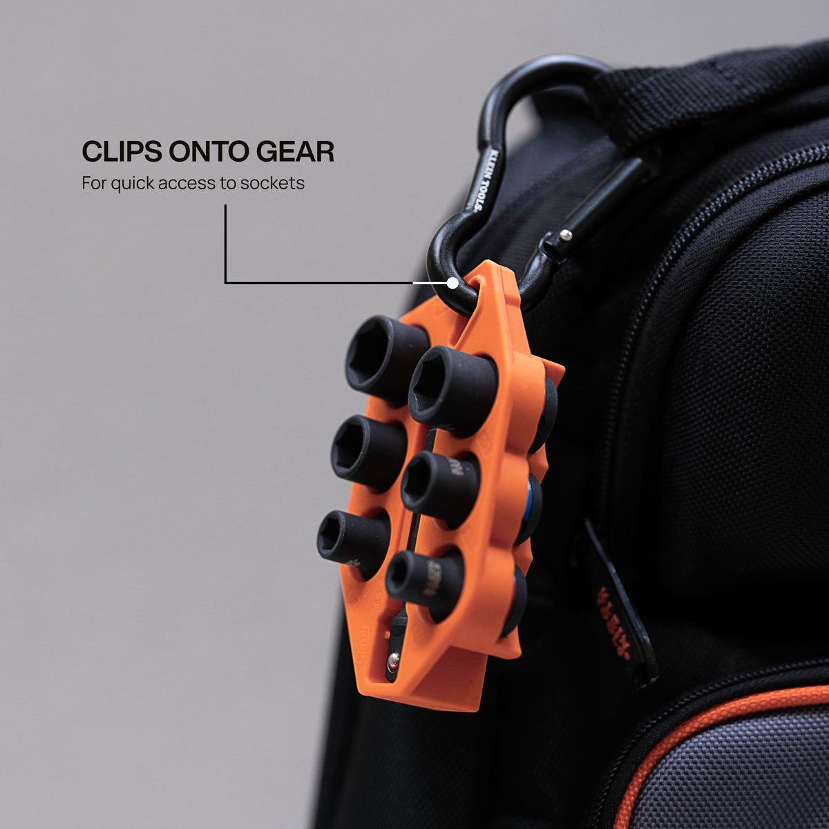 Klein Grab-And-Go socket holder clipped onto a tool backpack using an aluminum carabiner to demonstrate portable jobsite storage.