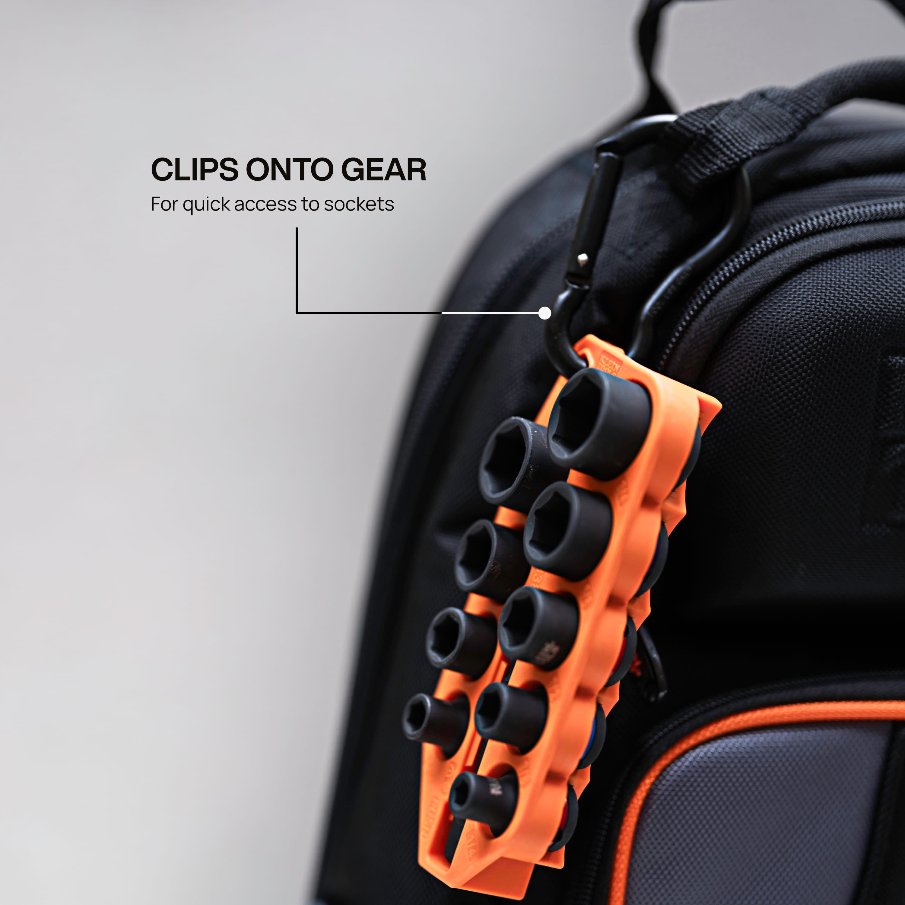 Klein Grab-And-Go socket caddy clipped onto a tool backpack using an aluminum carabiner to demonstrate belt and bag portability.