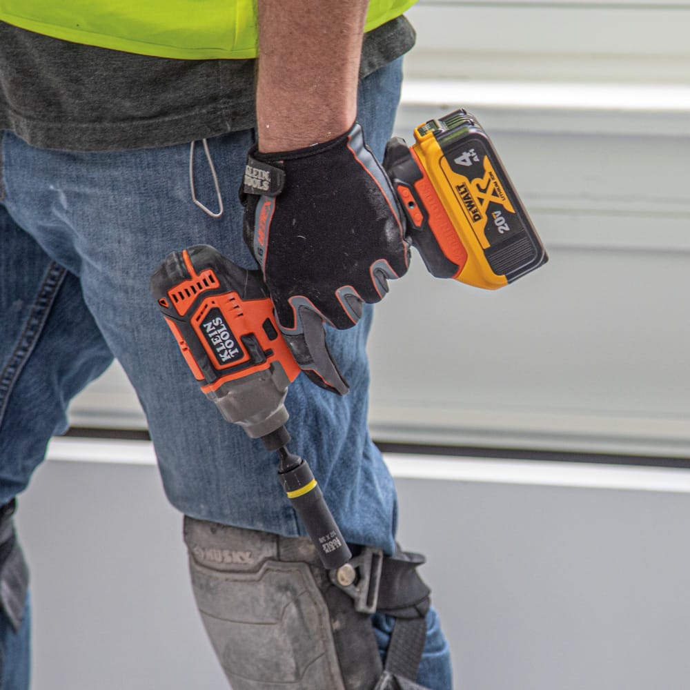 Gloved contractor holding a cordless impact driver equipped with a Klein coaxial socket to demonstrate tool belt portability.