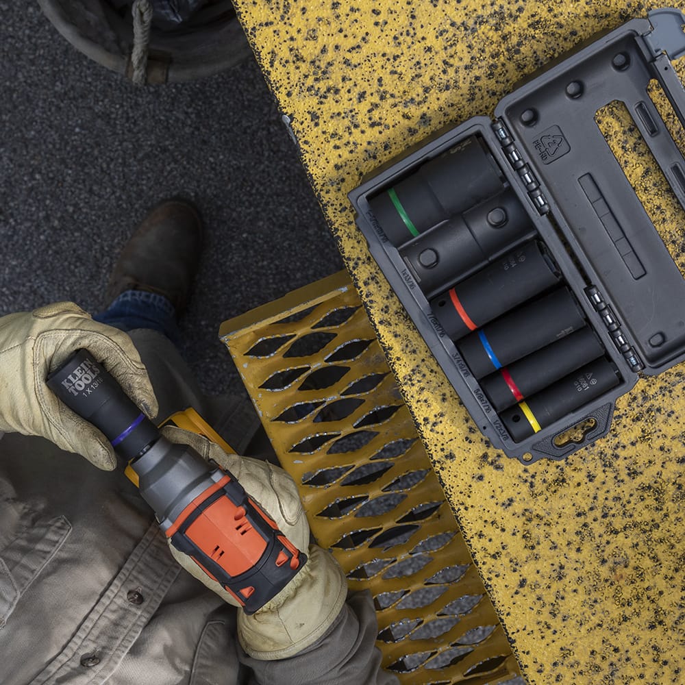 Overhead view of a gloved technician attaching a Klein coaxial socket to a 1/2-inch impact wrench on a bucket truck platform.